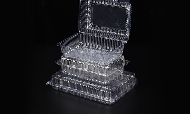 Stacked clear PET hinged clamshell containers for fruit on dark background
